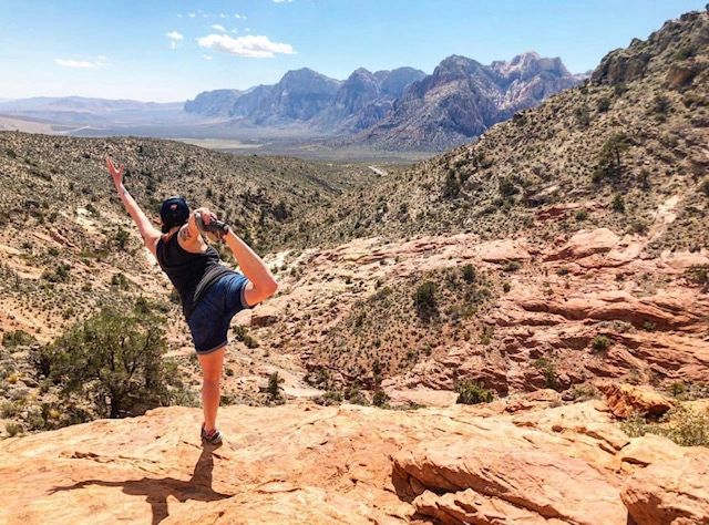 Person practicing yoga on a rocky mountain with scenic desert landscape.