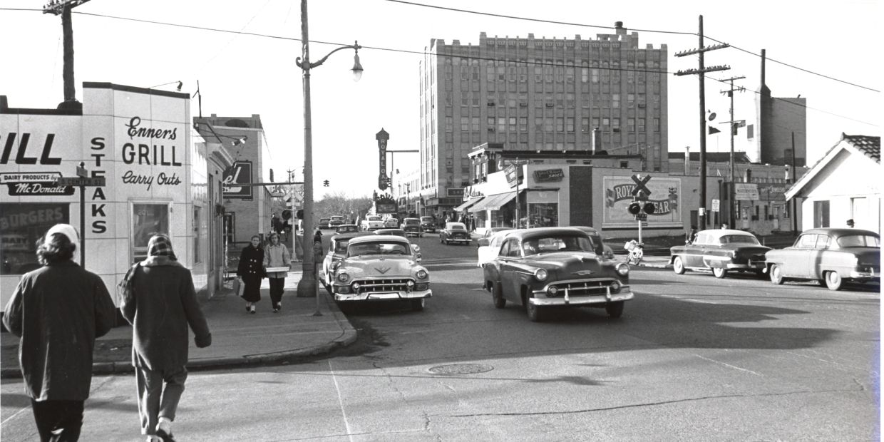Vintage street scene with classic cars and pedestrians in front of Enners Grill.