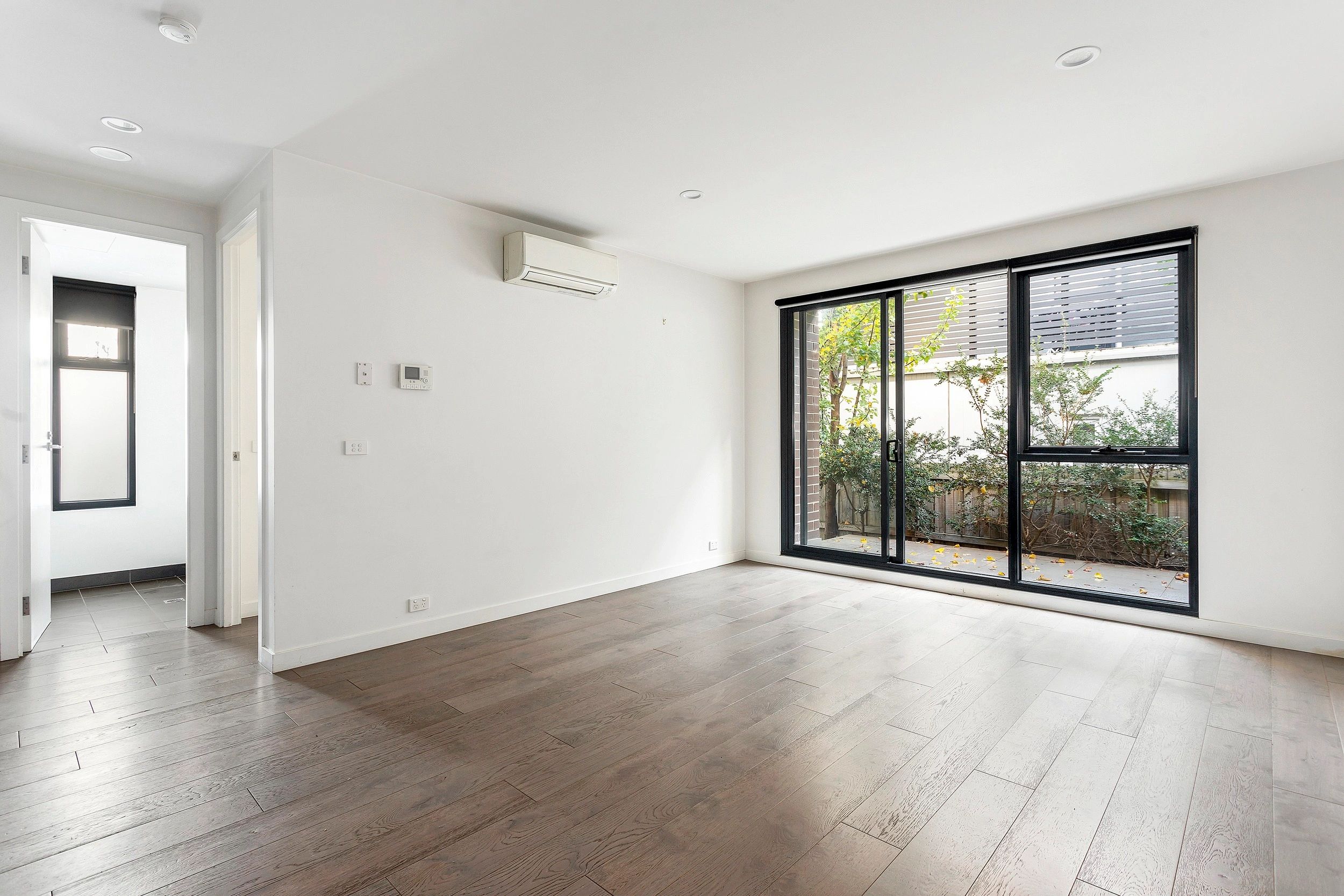 Empty modern room with wood flooring and large glass doors.