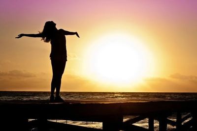 A silhouette of a person making an inspirational gesture with a rising sun in the background.