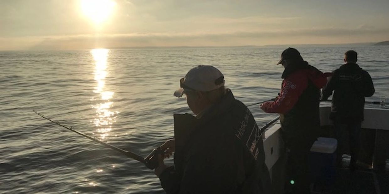 an evening photo with the sun setting and three fisherman fishing off the stern of the boat at falmo