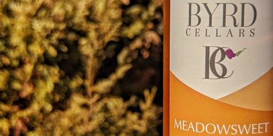 bottle of Byrd Cellars Meadowsweet strawberry apple wine in front of bush background