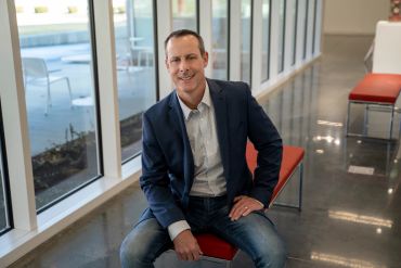 Man in business casual attire sitting on a red bench indoors.