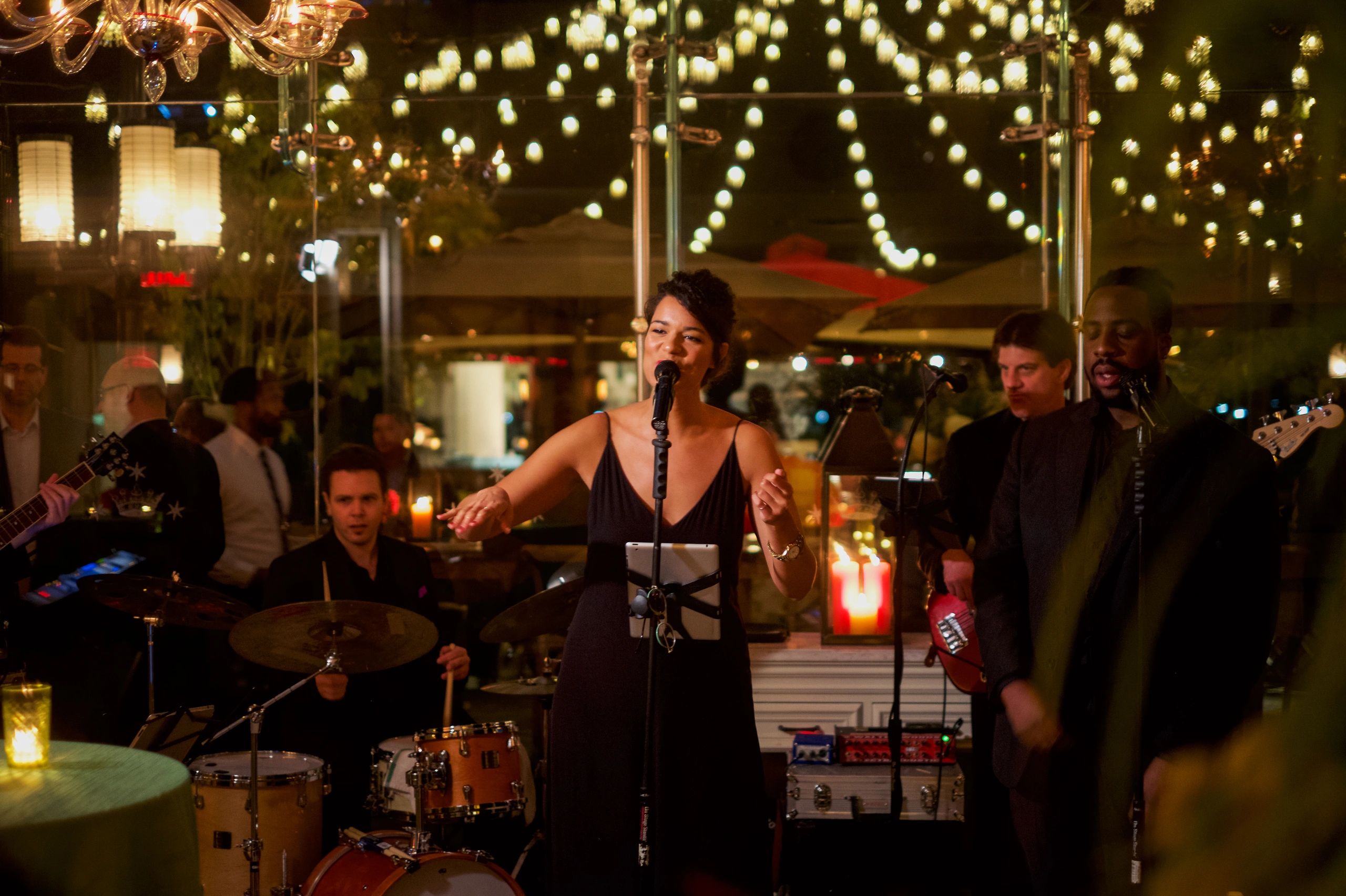 A female singer performs with a live band in a warmly lit venue.