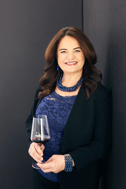 Founder of Wines of Illyria, Indira Bayer, in a suit jacket and blue top wearing a lapis necklace. 