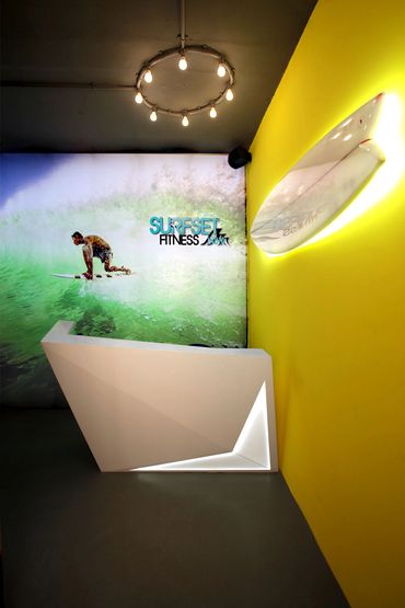 Modern fitness reception with surfboard decor and vibrant yellow wall.