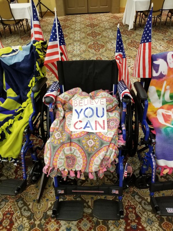 Wheelchair decorated with American flags and a motivational sign.