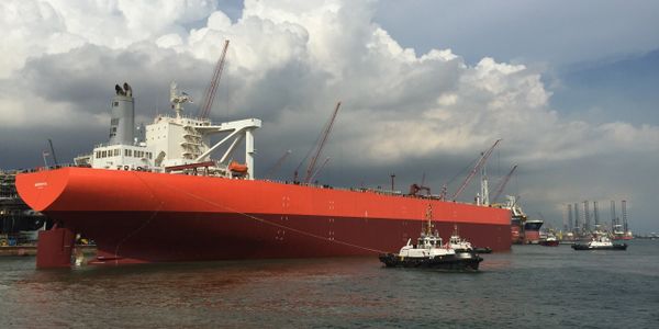 Red oil tanker ship towed by tug boats at yard in Singapore