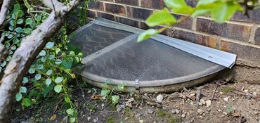 Frosted sloped window well cover for basement protection, privacy, and water drainage.