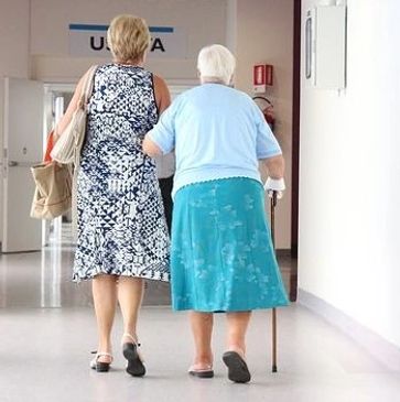 Elderly woman with cane holding on to another woman for help walking to medical appointment