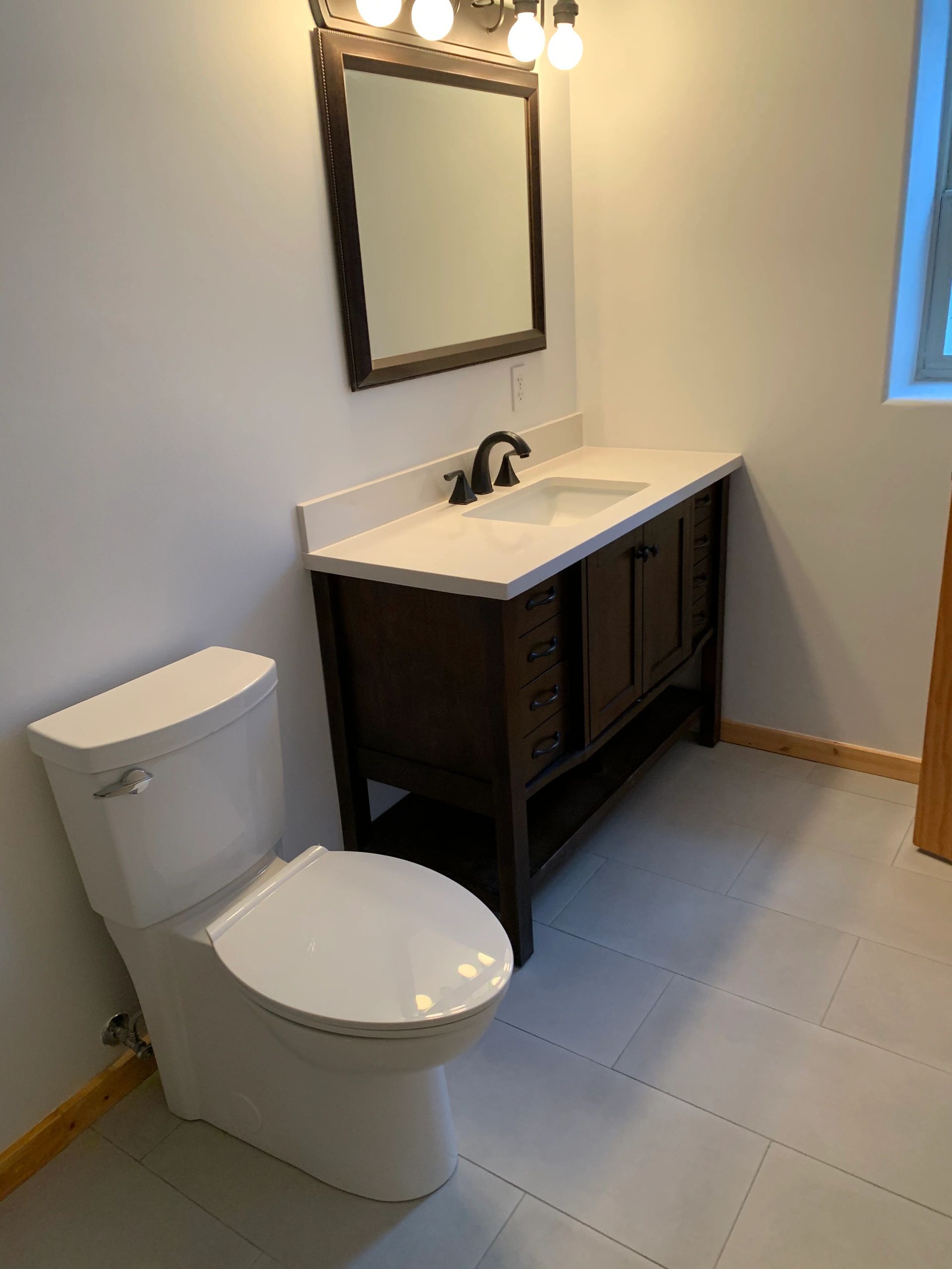 Toilet, medicine cabinet, light fixtures, vanity, tiled bathroom floor installation. Heated bathroom