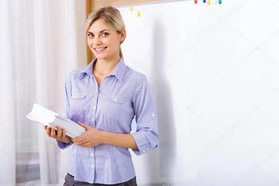 Smiling woman holding books in front of a whiteboard.