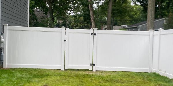 White vinyl fence with grass in front and trees behind.
