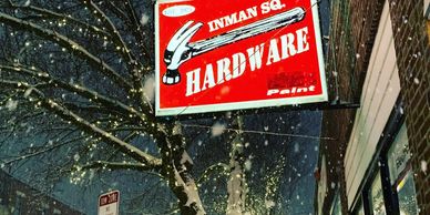 Photo of the Inman Square Hardware blade sign lit up and glowing on a snowy night