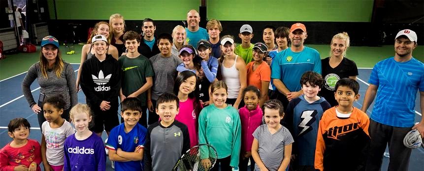 Group photo of diverse tennis players and coaches on an indoor court.