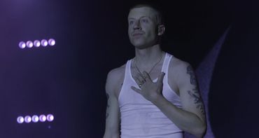 Man in a white tank top on stage under purple lighting.