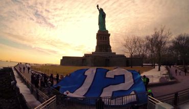 A large 12th man Seahawks flag displayed near the Statue of Liberty at sunset.