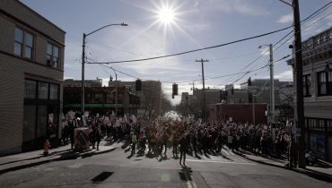 Crowd gathers under bright sun at city intersection during event or protest.