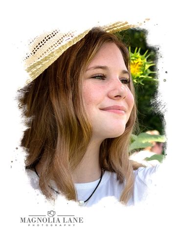 Outdoor portrait of a young girl with long blonde hair wearing a hat in the sunflower patch.