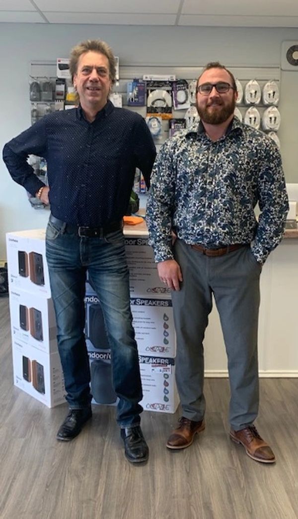Two men standing in front of stacked speaker boxes in a store.