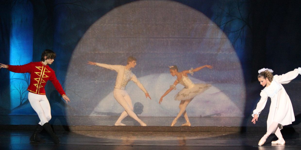 Ballet dancers performing under a spotlight on stage.