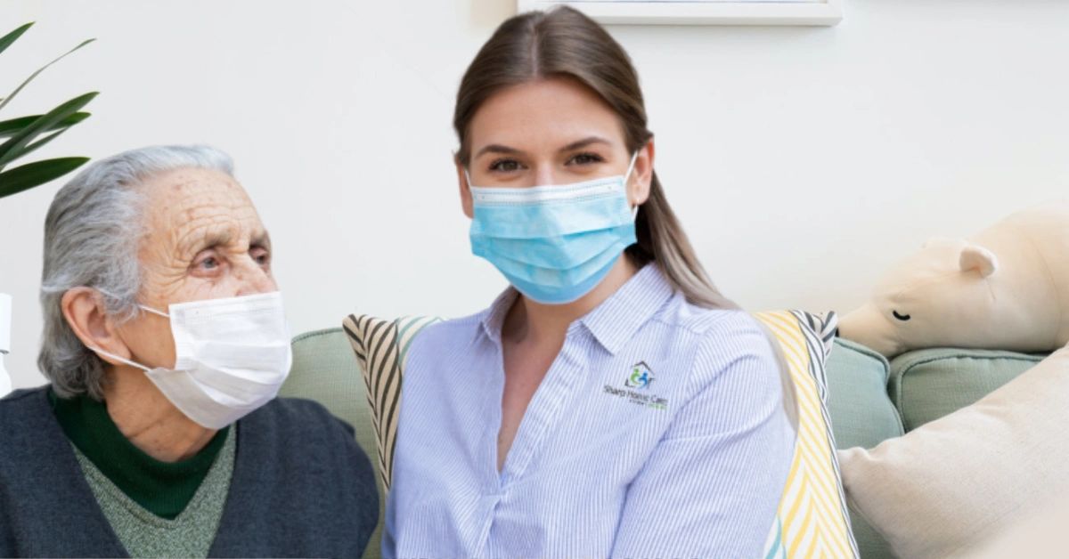 Elderly woman with Sharp Home Care caregiver, both wearing masks.