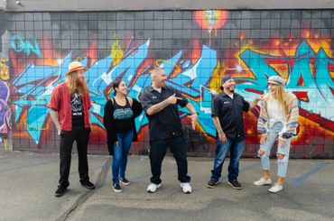 Five people standing with a graffiti wall behind