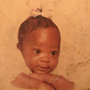 A baby with a white bow on head and bracelet on arm.