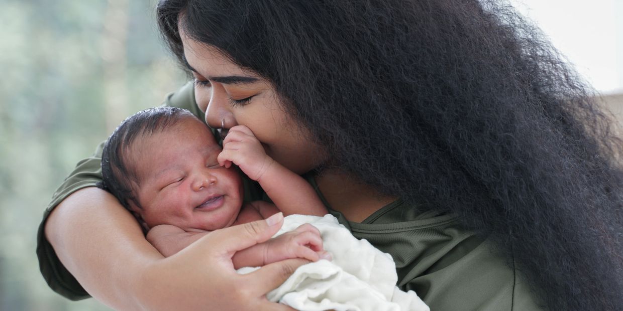 Photo of a person with long curly black hair kissing and cradling a newborn.