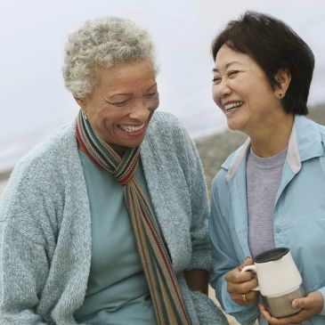 Two older women laughing and sharing a moment outdoors.