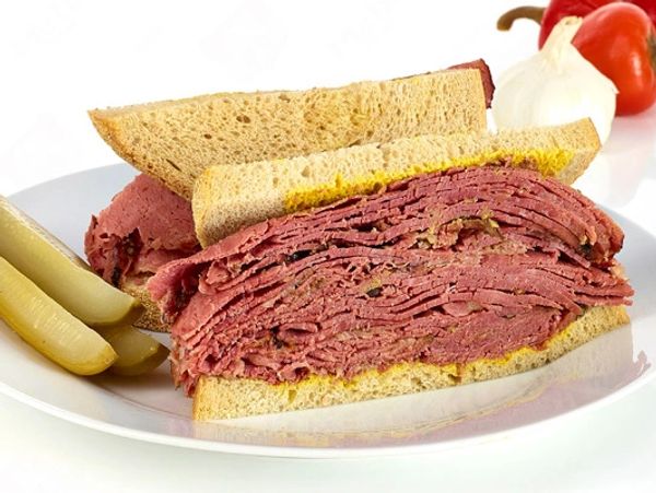 A pastrami sandwich with pickles on a white plate.