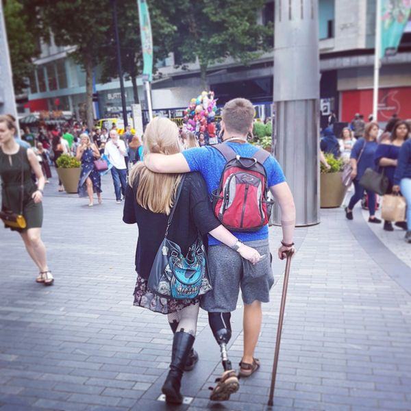 Pete walking away through busy street with walking stick and arm around wife