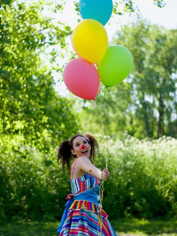 Clown joyeuse en robe arc-en-ciel avec des ballons colorés, animation extérieure pour enfants