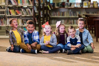 6 elementary age special needs children sitting on floor in a library. All are smiling and laughing 