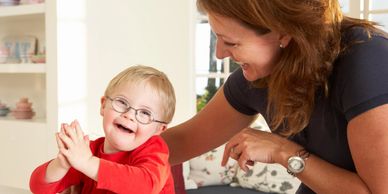 Female Speech Language Therapist sits next to child with Down's Syndrome. Child smiles and claps