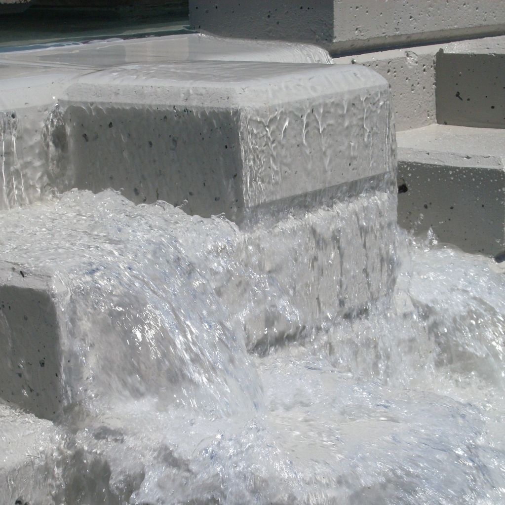 Water flowing over a cement waterfall from upper fountain to lower fountain.