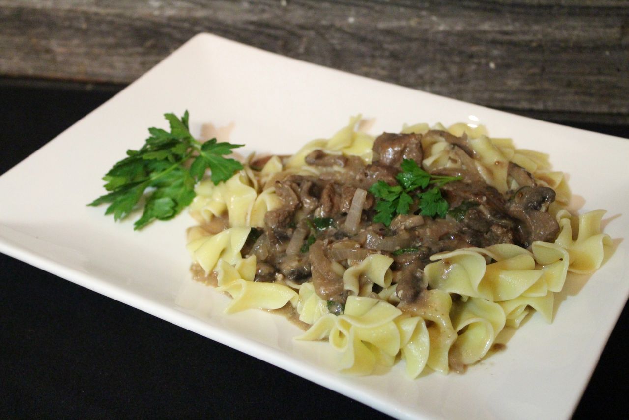 Bison stroganoff on egg noodles served on a square white plate