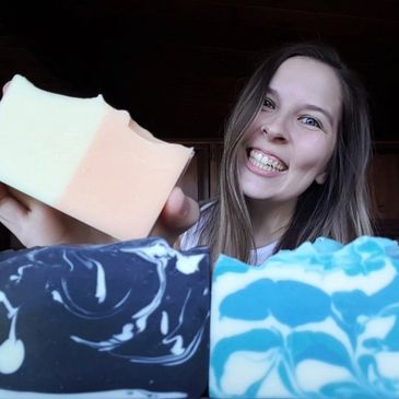 Young woman smiling holding a handmade vegan soap with two colourful  soap bars in the forefront