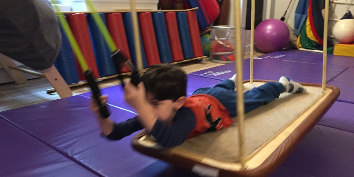 A child swinging on a rectangular swing in an indoor play area.