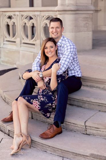 He is hugging his fiance, while sitting on stone steps. 