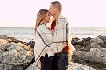 Kissing her forehead wrapped in a blanket on the rocks by the beach. 