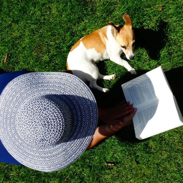 Person laying in grass reading with small dog.