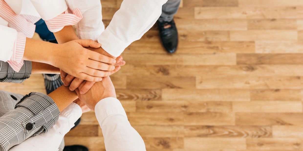 Hands of several sales people in a huddle.