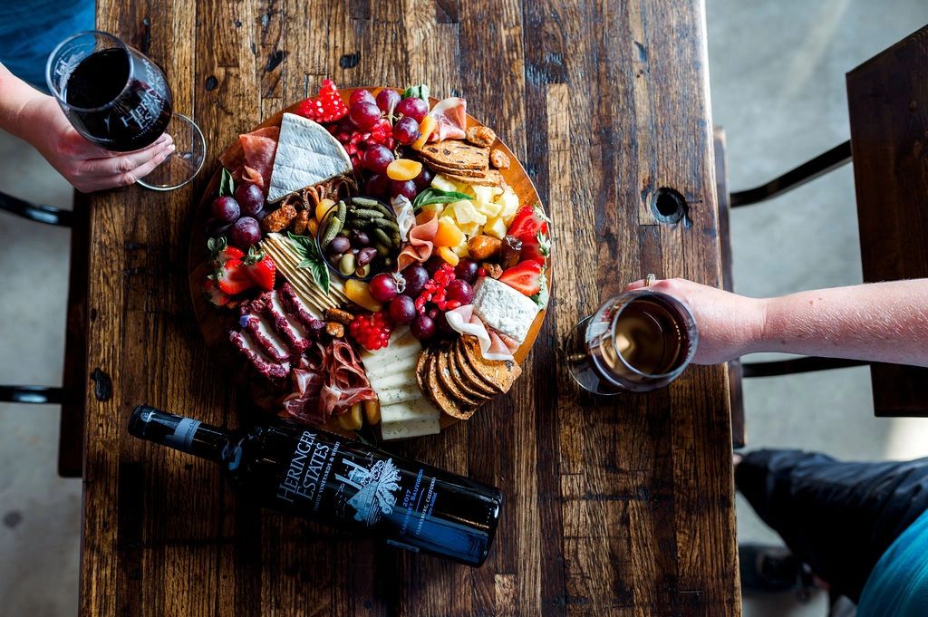 Image of table with platter of food two hands holding glasses of wine and wine bottle with Heringer 