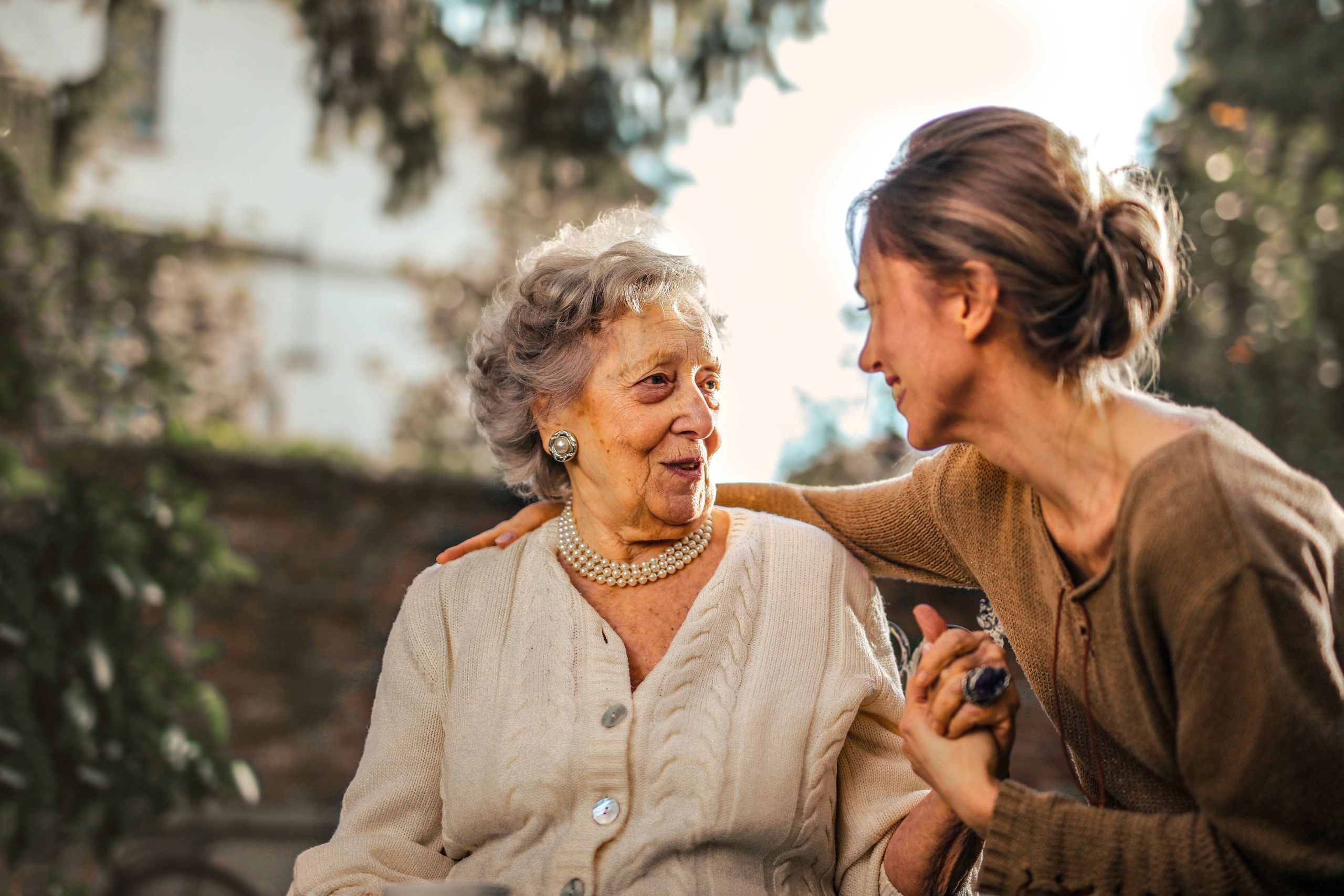 Daughter with elderly mother wearing sweater, sitting outside on a bench, holding hands