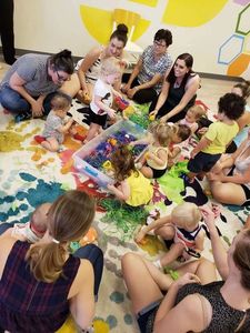 Women and children gather around a  sensory bin with colorful toys