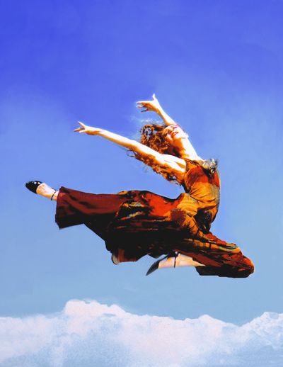 Woman joyfully leaping in the air against a blue sky.