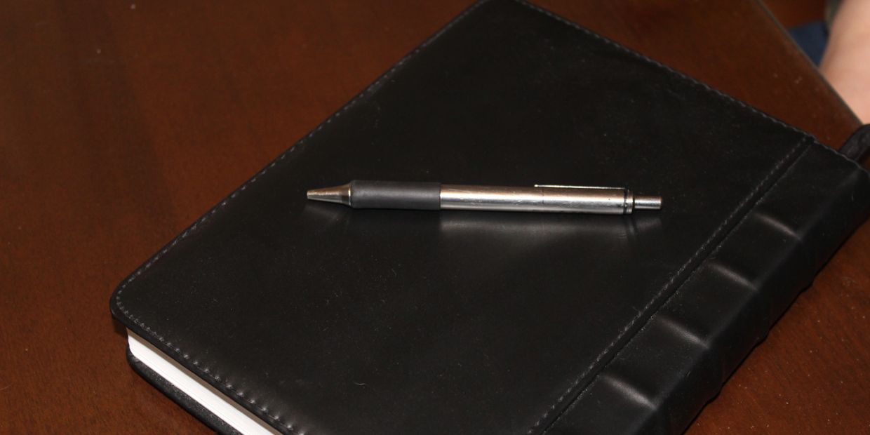 Closed notebook with a pen resting on top.