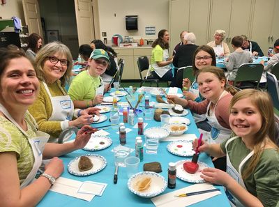 Group of people enjoying a pottery painting activity indoors.
