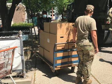 Military personnel transporting boxes on a cart outdoors.